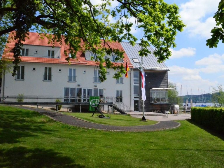 Ein modernes Gebäude mit roten Dächern, umgeben von Rasen und Bäumen, am Ufer eines Sees gelegen.